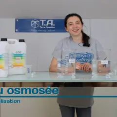Une femme souriante présente des produits pour ajuster le pH de l'eau osmosée, avec des béchers et des bouteilles sur une table.