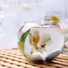 Comment décorer un grand vase en verre transparent : une fleur blanche flottant avec des galets et une bougie allumée.