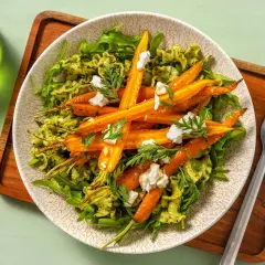 Pâtes au pesto avec des carottes rôties et des éclats de fromage de chèvre, garnies de fanes de carottes fraîches.