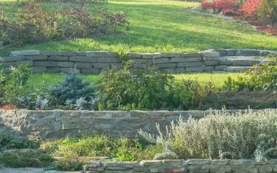 Aménager une butte de terre en pente avec des murets de pierre et des plantations variées, créant des terrasses verdoyantes.