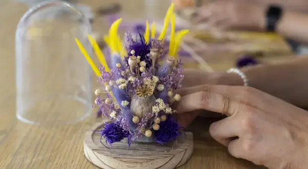 Un bouquet de fleurs séchées aux tons violets et jaunes, prêt à être protégé sous cloche. Un atelier créatif pour composer de jolies décorations.