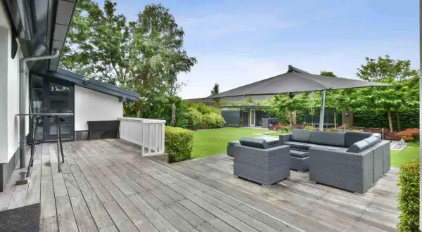 Aménagement coin détente extérieur avec salon de jardin gris sous un grand parasol, sur une terrasse en bois.