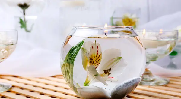 Comment décorer un grand vase en verre transparent : une fleur blanche flottant avec des galets et une bougie allumée.