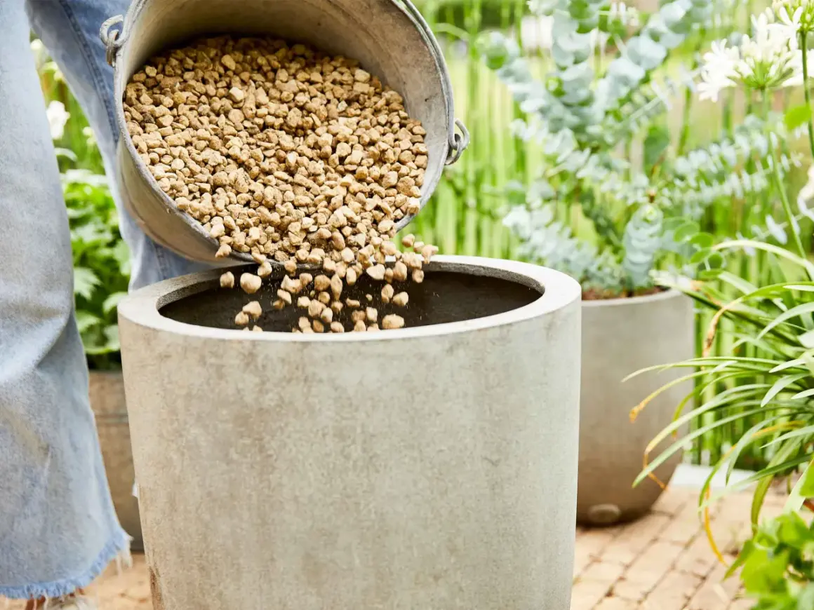 Une personne verse des billes d'argile dans un pot en béton, préparant un substrat plante intérieur.