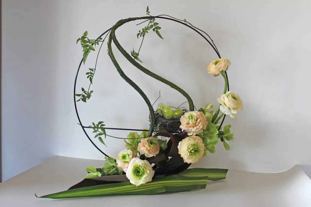 Composition florale avec des renoncules, des œufs verts dans un nid, et une feuille symbole de renouveau.