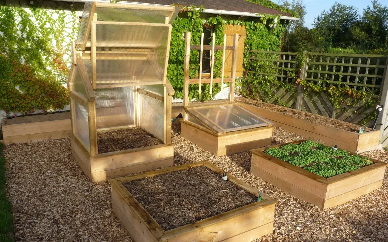 Plusieurs carrés potagers en bois, certains avec des mini-serres, sont prêts à l'emploi dans un jardin.