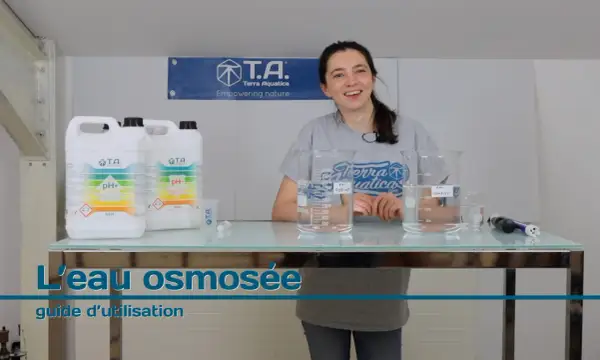Une femme souriante présente des produits pour ajuster le pH de l'eau osmosée, avec des béchers et des bouteilles sur une table.