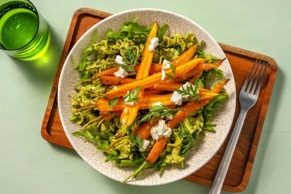Pâtes au pesto avec des carottes rôties et des éclats de fromage de chèvre, garnies de fanes de carottes fraîches.